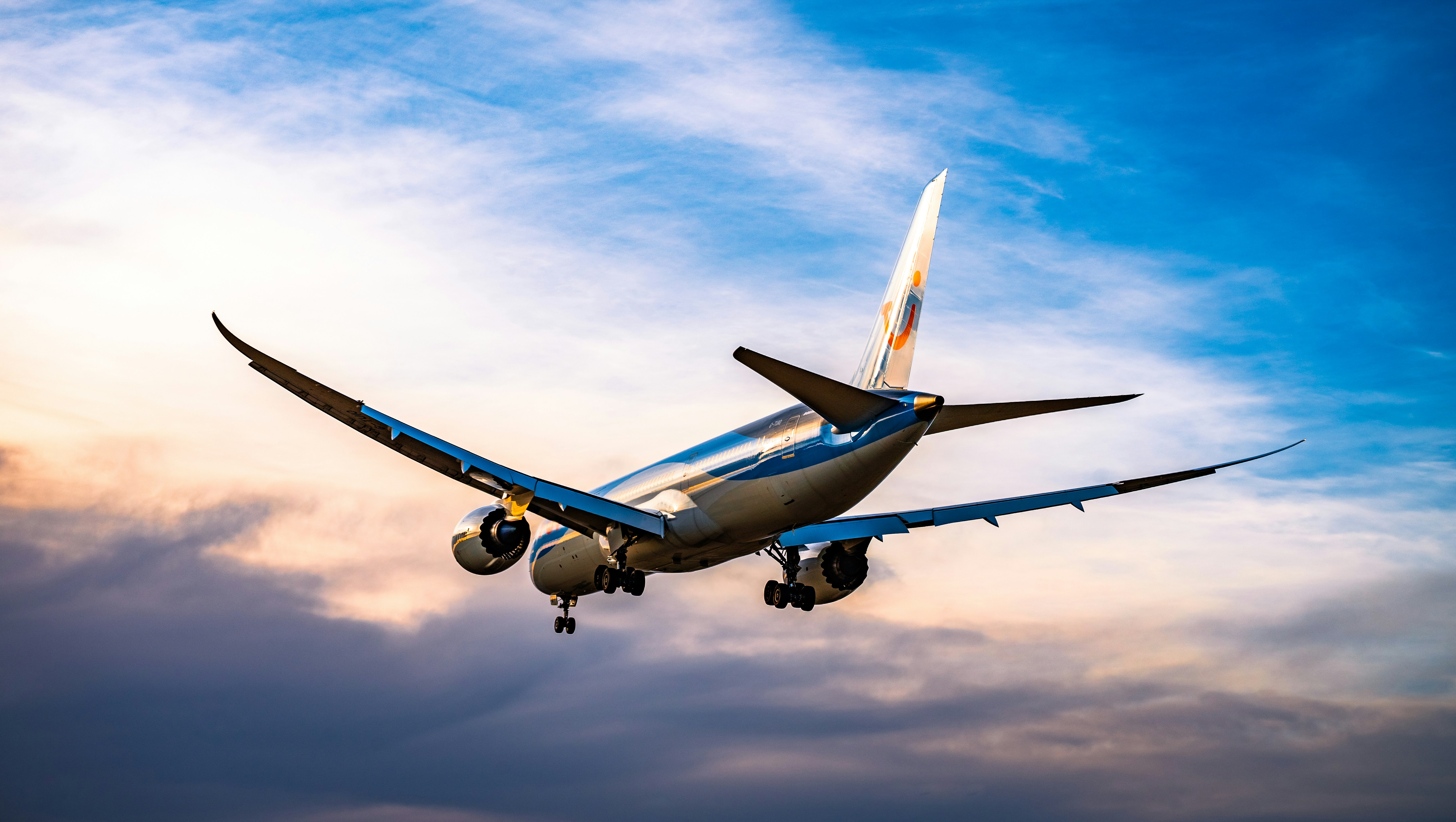 Boeing 787 widebody on final approach at sunset, gear extended, twilight sky dividing warm and cool light.