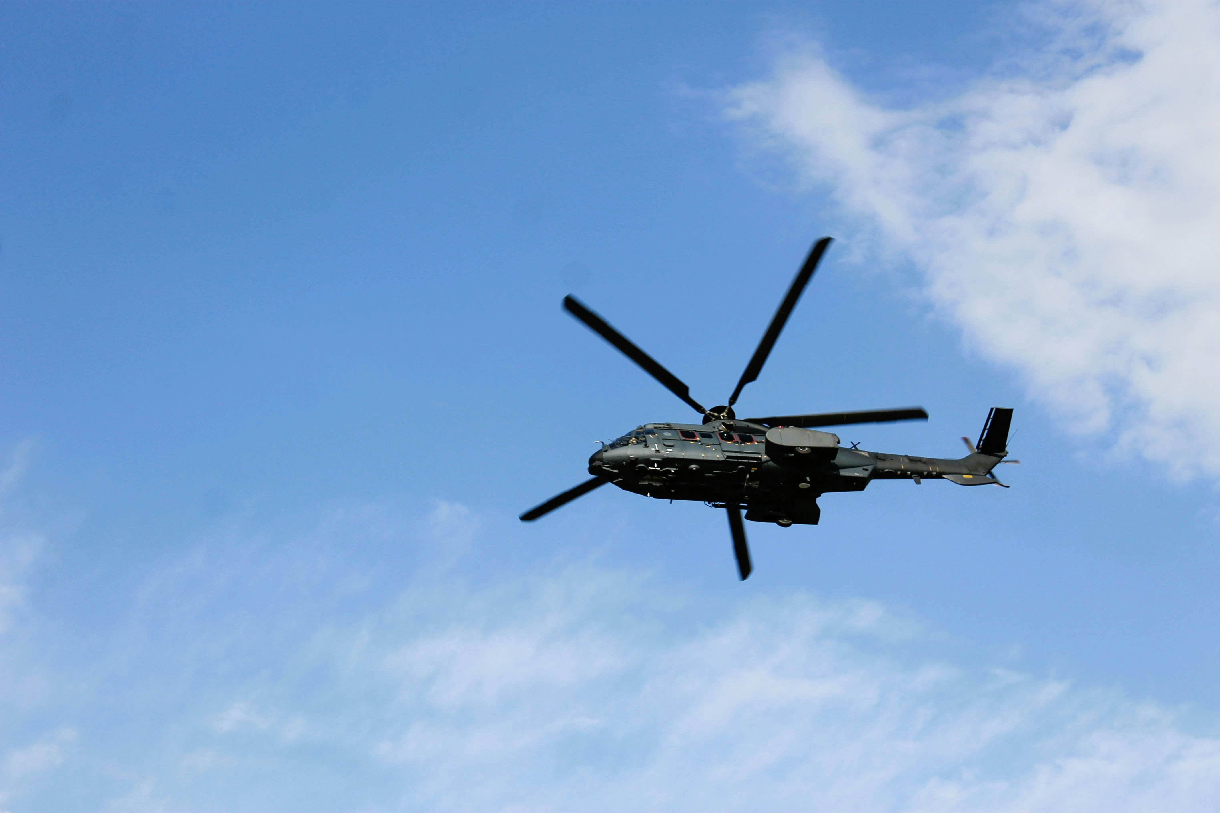 Medium-lift military rotorcraft in level flight against a clear blue sky, main rotor caught mid-rotation.
